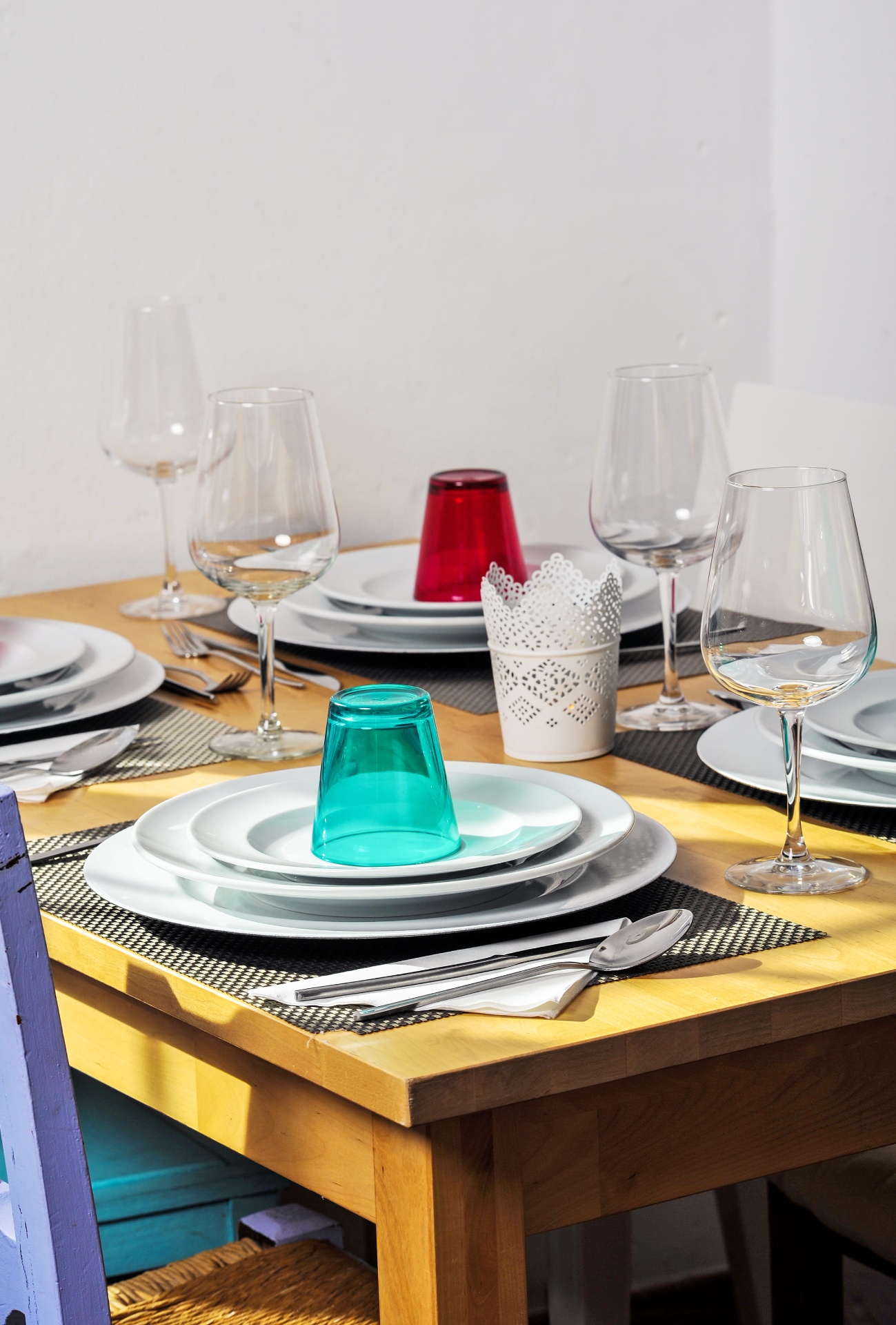 Mesa posta com louça branca, copos coloridos e talheres