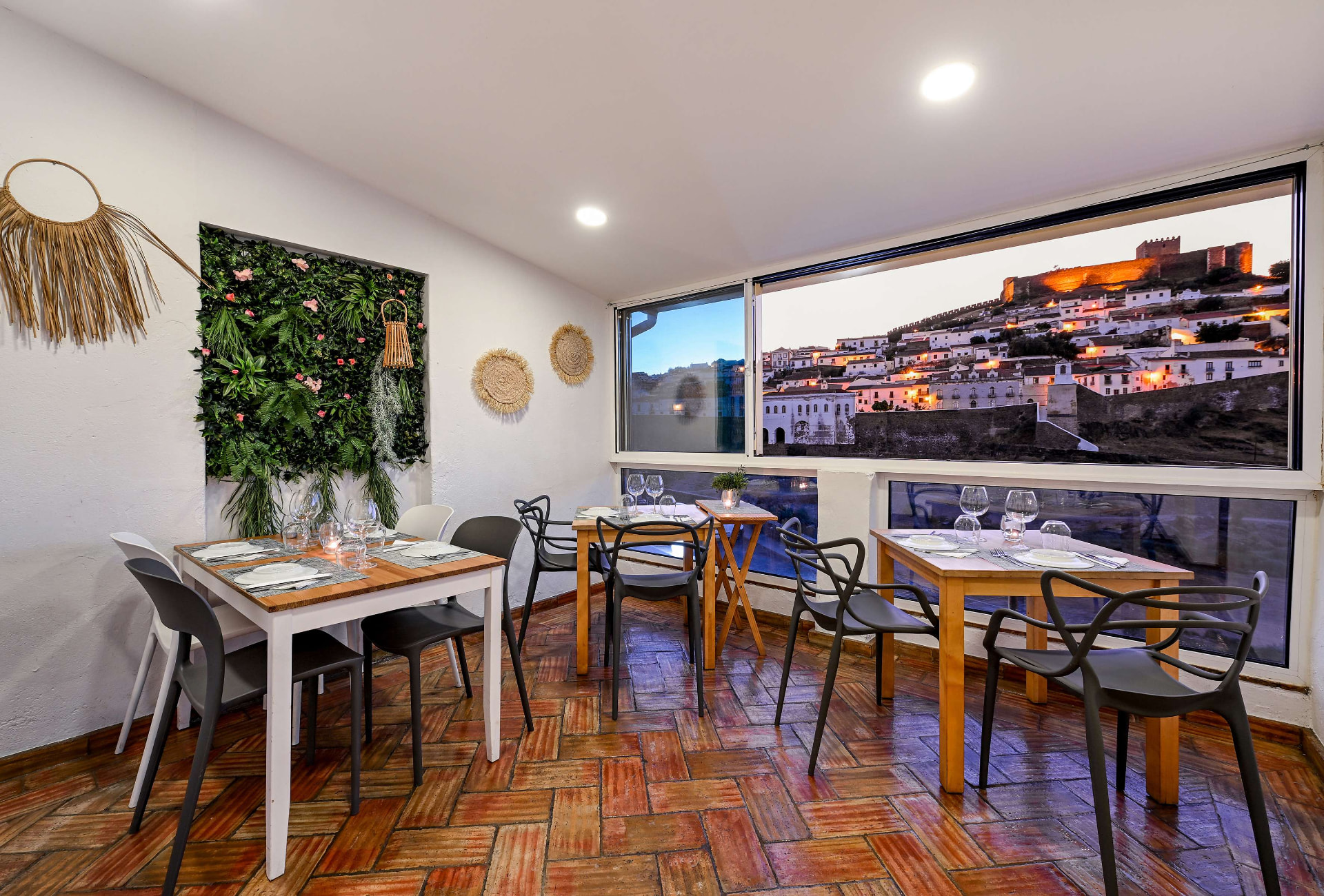 Sala do restaurante ao anoitecer com jardim vertical e janela panorâmica sobre o castelo de Mértola