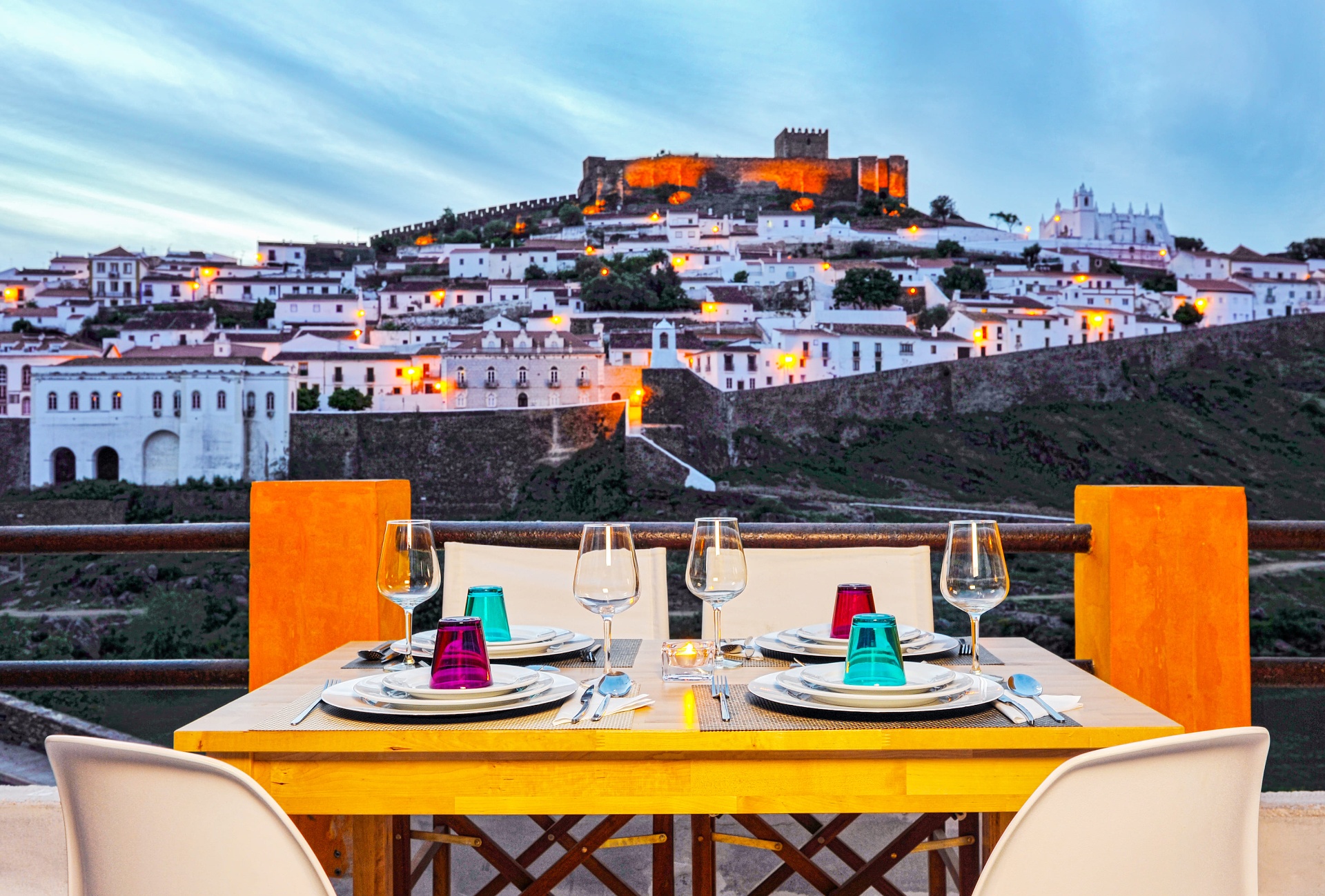 Mesa posta na esplanada da Casa Amarela com vista para o castelo e vila branca de Mértola ao entardecer