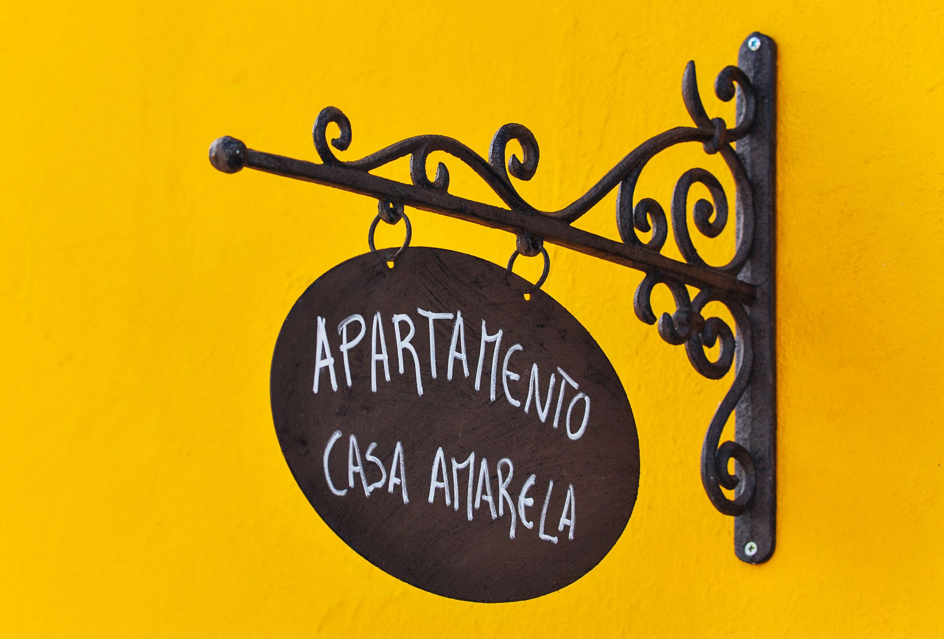 Tabuleta artesanal do Apartamento Casa Amarela em ferro forjado sobre fachada amarela