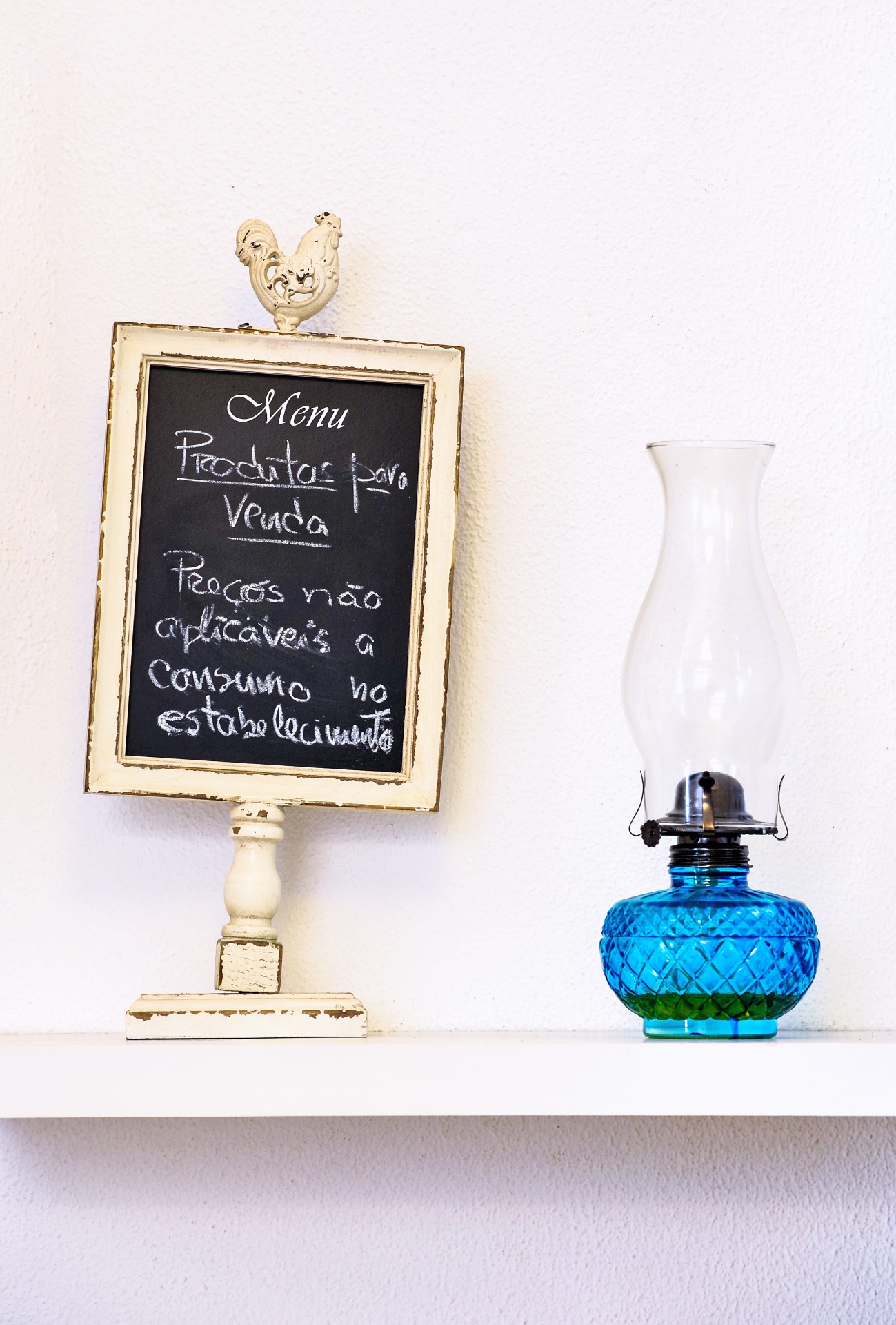 Ardósia decorativa com menu de produtos para venda junto a candeeiro a petróleo azul