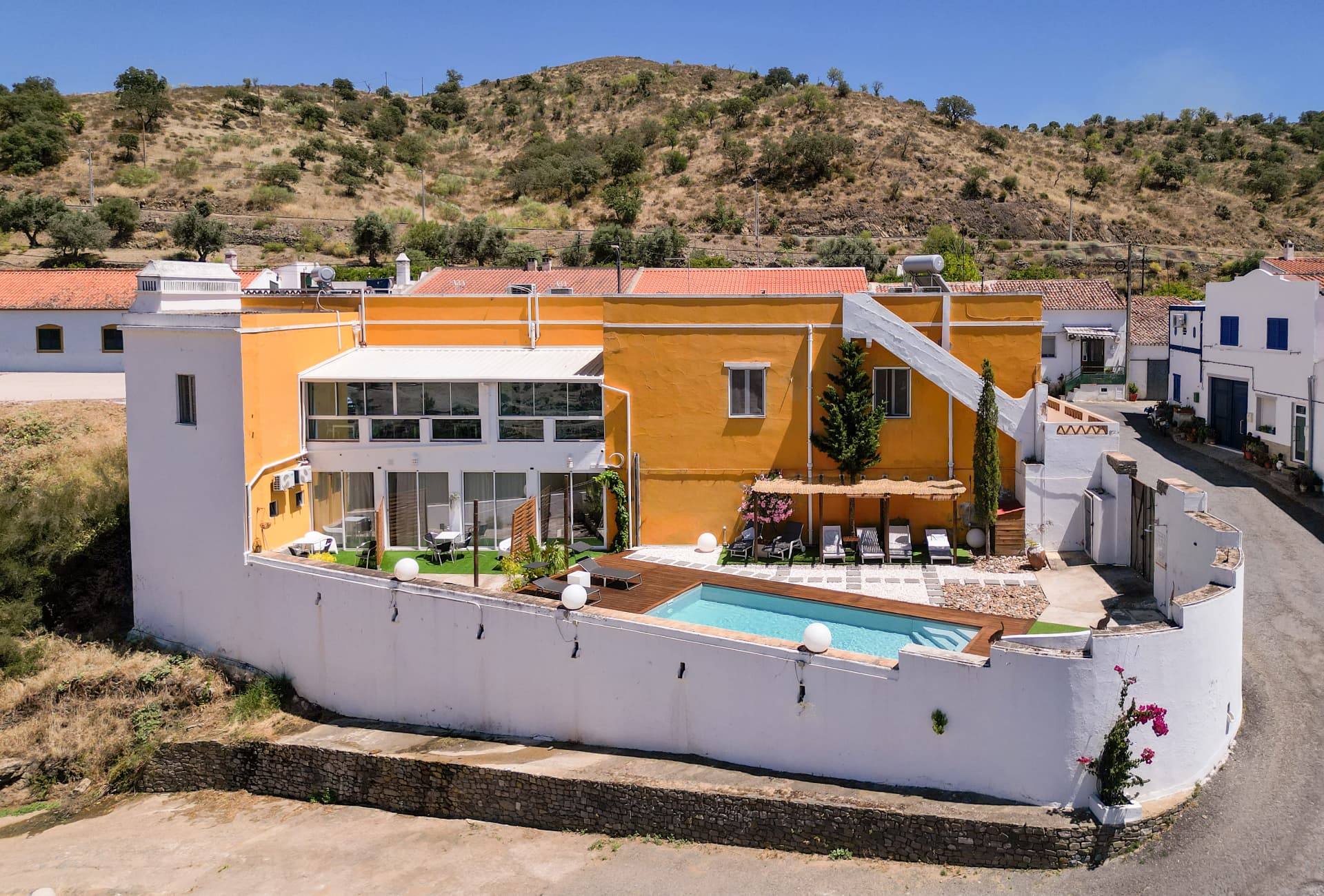 Vista aérea da Casa Amarela, com a fachada amarela, a sala envidraçada e a piscina, sobre a encosta do Guadiana